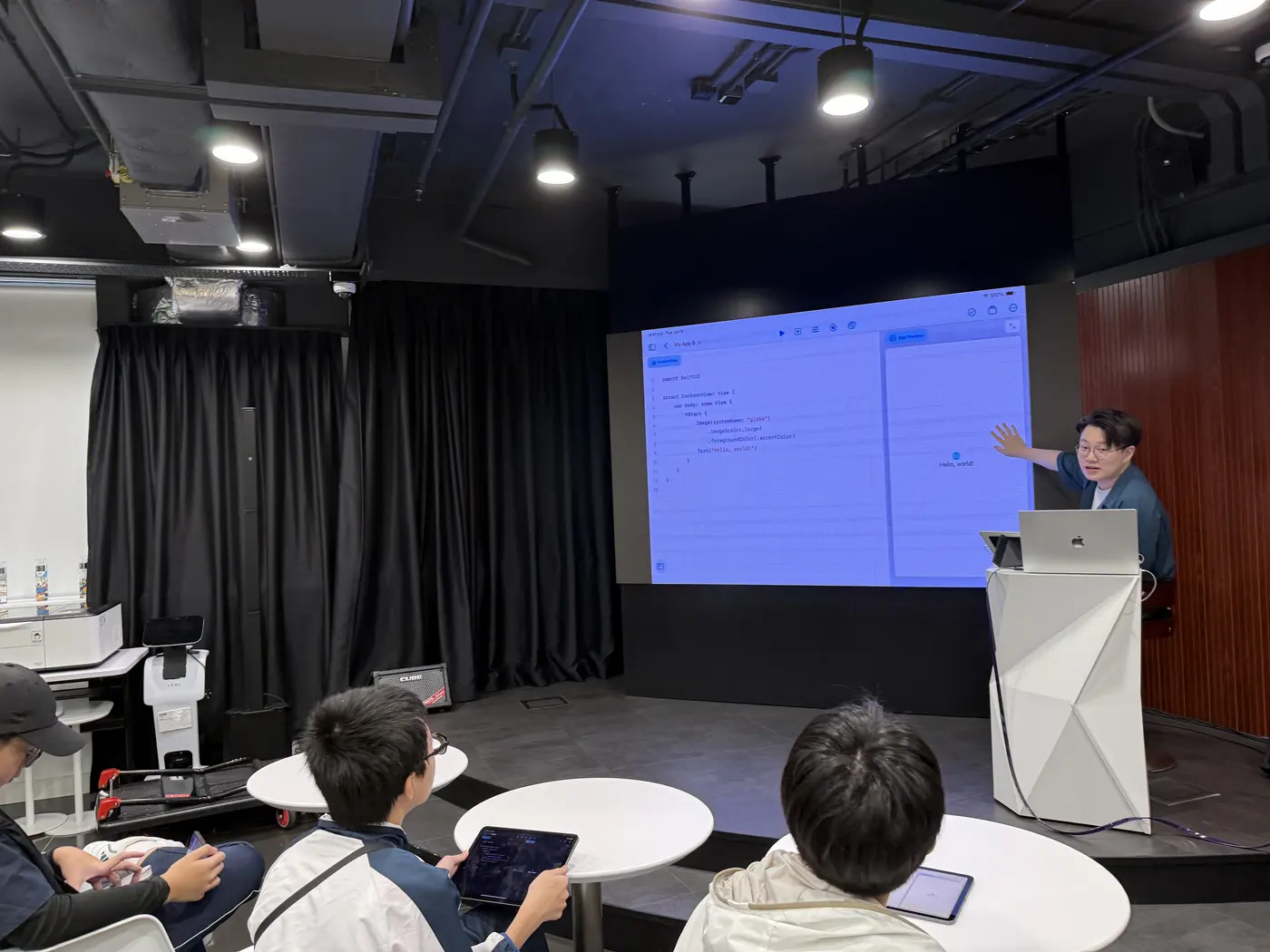 A tutor explaining on stage while students follow along on iPads