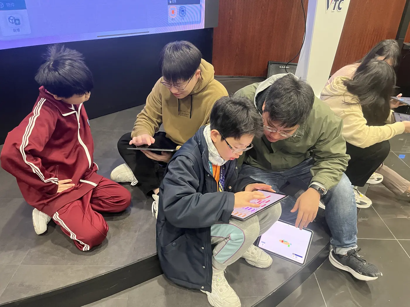 A tutor sitting on the floor with students, creating together on iPads